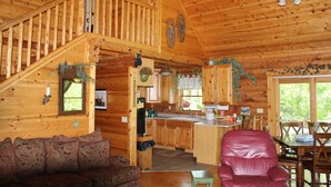Ein Holzblockhaus-Innenraum mit Treppe, einem Wohnzimmer mit Sofa, einer Küchenzeile und einem Esstisch mit Stühlen.