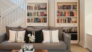 Un salon avec un canapé gris, des coussins blancs et noirs, et une bibliothèque remplie de livres.