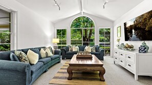 A spacious living room with a large wooden coffee table, two sofas, and a view of lush greenery through large windows.