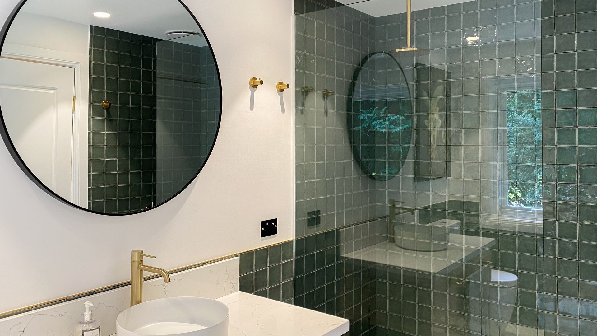 A modern bathroom with a round mirror, a white sink, and a glass-enclosed shower.