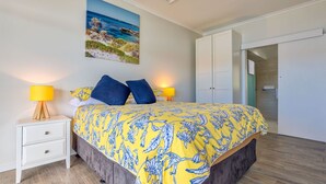A bedroom with a bed, two bedside lamps, a nightstand, a wardrobe, and a painting of a beach scene.