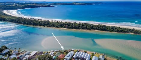 An aerial view of a coastal residential area with houses, a beach, and clear blue waters.