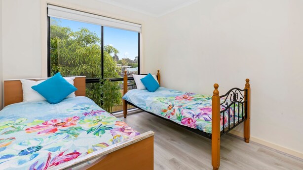 Dos camas individuales con ropa de cama floral, una ventana con vistas a la vegetación y una barandilla de balcón.