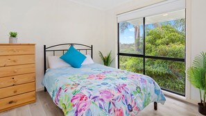 A bedroom with a bed, a wooden dresser, and a large window with a view of greenery. - ROSEBUD GROUP GETAWAY (ROSEBUD)
