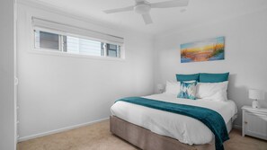 A bedroom with a bed, a nightstand, a painting, a ceiling fan, and a window. - Sunsets on Headland, Gerroa (Gerroa)