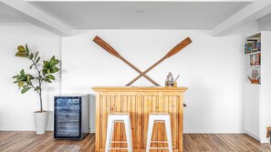 A room with a wooden bar area, two white stools, a potted plant, and a bookshelf. - Sunset on Headland, Gerroa (Gerroa)