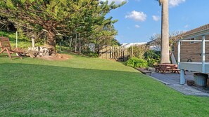 A well-maintained backyard with a grassy lawn, a tall palm tree, and a wooden bench. - Sunsets on Headland, Gerroa (Gerroa)