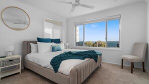 A bedroom with a bed, a nightstand, a chair, a large window with a view, and a ceiling fan. - Sunset on Headland, Gerroa (Gerroa)