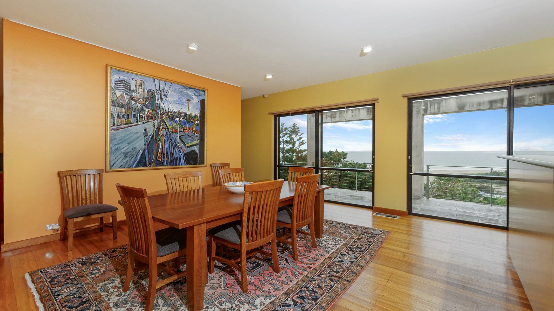 A dining area with a wooden table, six chairs, and a large painting on the wall.