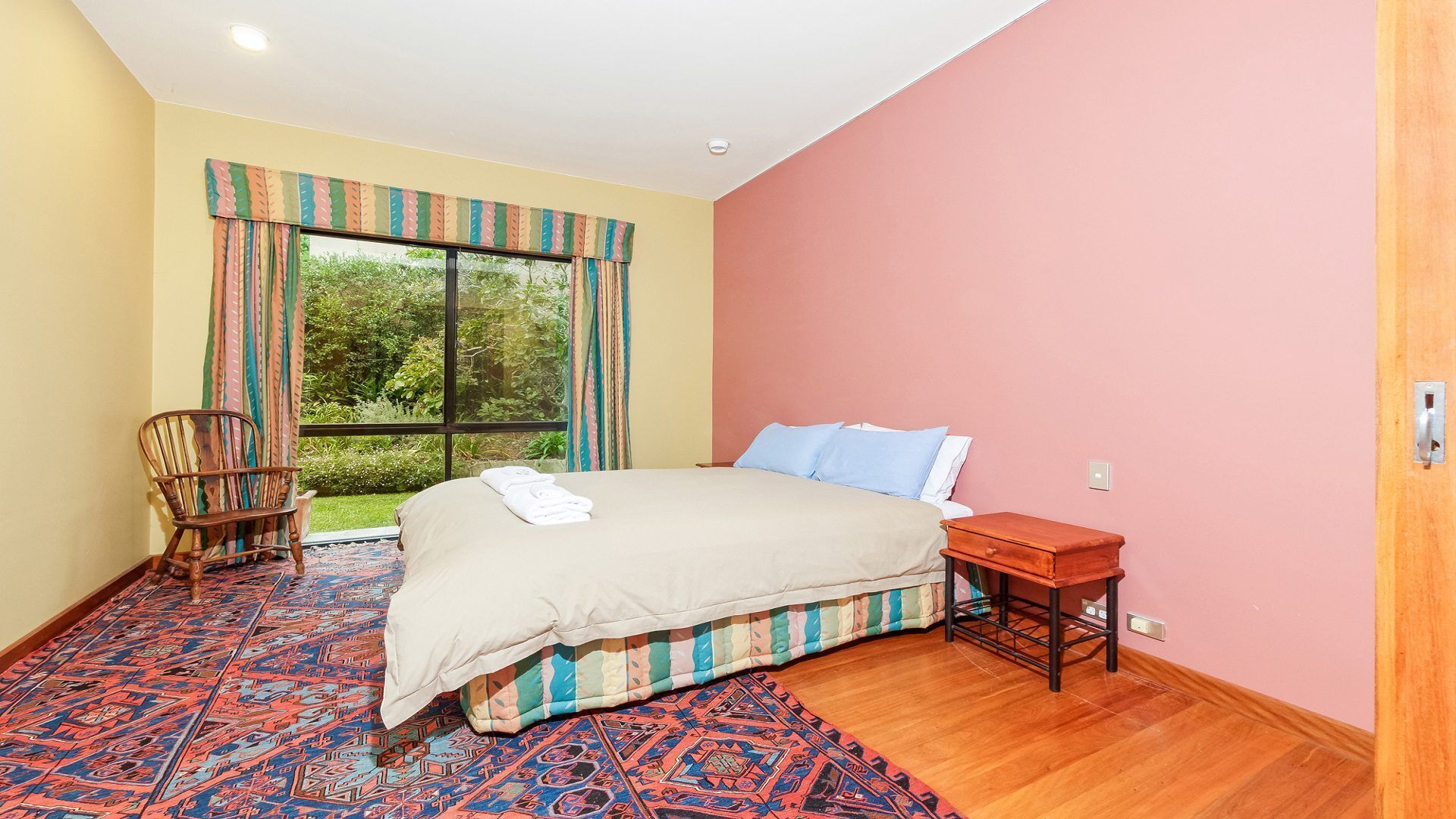 Een slaapkamer met een bed, een stoel, een nachtkastje en een raam met gordijnen.