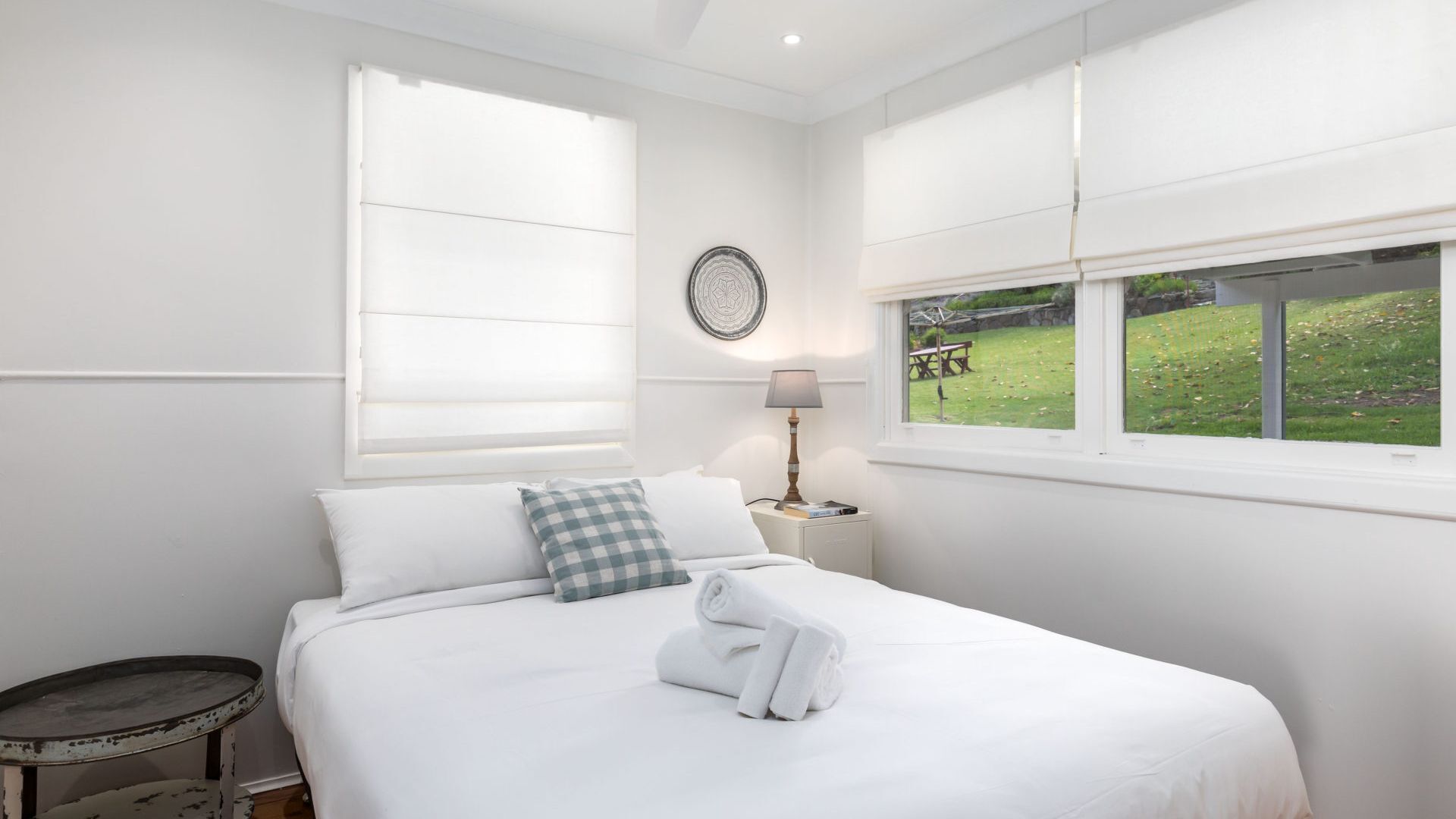 Una camera da letto con un letto, un comodino con una lampada, un elemento decorativo rotondo a parete e una finestra vista su una zona erbosa.