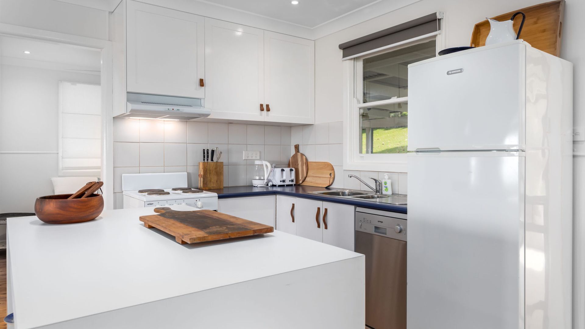 Une cuisine moderne avec des meubles blancs, un îlot central, une cuisinière, un évier et un lave-vaisselle.