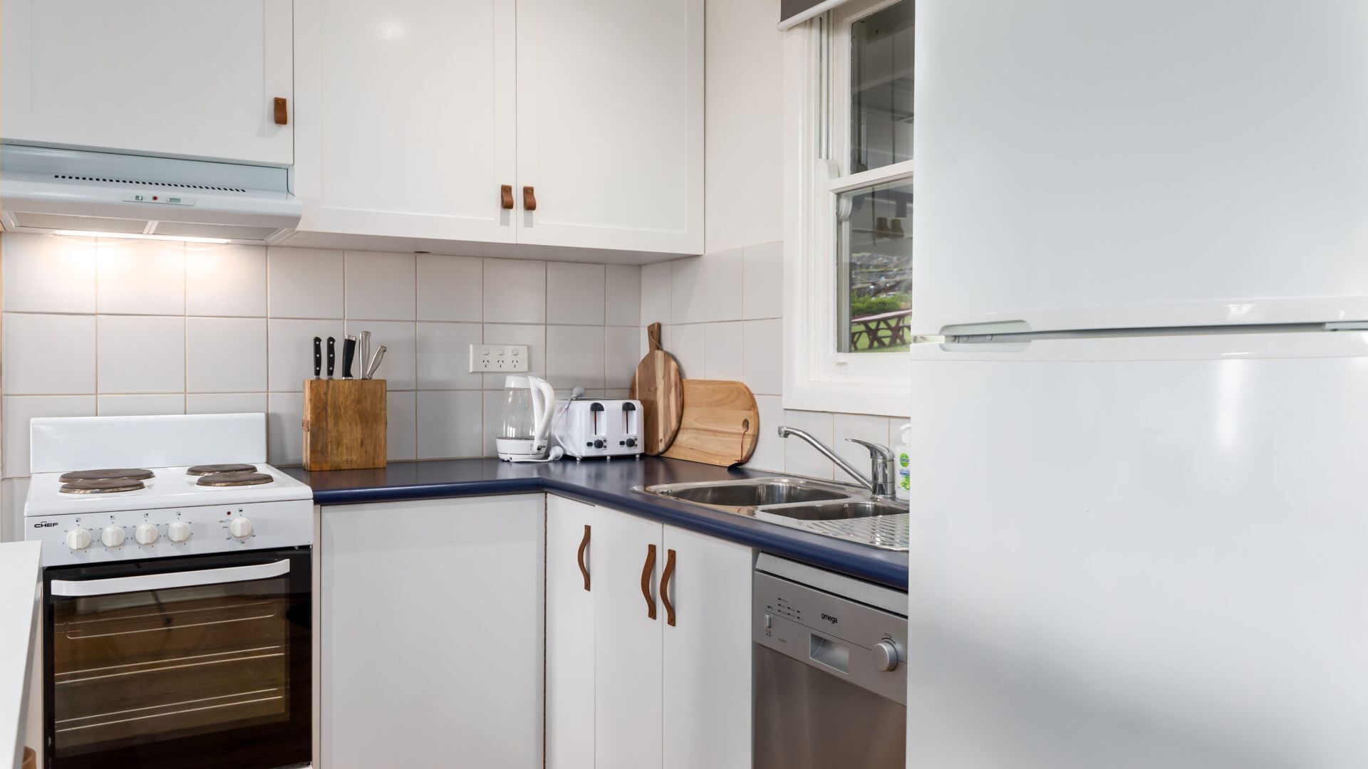 Une cuisine moderne avec des meubles blancs, une cuisinière, un lave-vaisselle et une fenêtre.