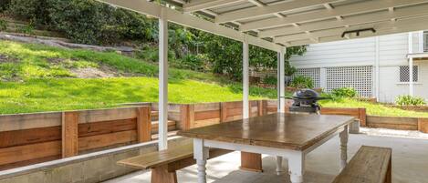 An outdoor patio with a wooden table and benches, surrounded by a white pergola.