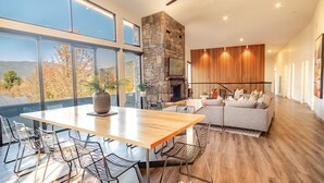 A modern living room with a stone fireplace, a dining area with a wooden table, and a sofa. - GLASS HOUSE: Bright Township (Bright)