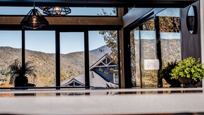 A modern interior with large windows, a hanging light fixture, and a view of a mountain and a building. - GLASS HOUSE: Bright Township (Bright)