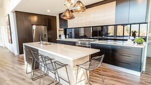 A modern kitchen with a large island, bar stools, a built-in oven, and pendant lighting. - GLASS HOUSE: Bright Township (Bright)