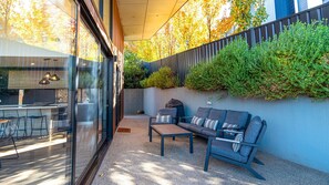 A modern outdoor seating area with a glass wall, a concrete wall with greenery, and a metal fence. - GLASS HOUSE: Bright Township (Bright)