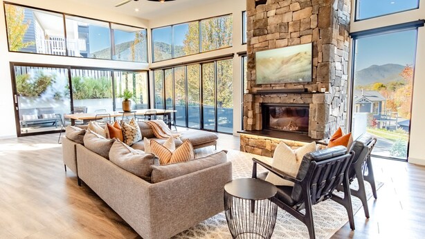A spacious living room with a stone fireplace, large windows, and a comfortable seating area. - GLASS HOUSE: Bright Township (Bright)