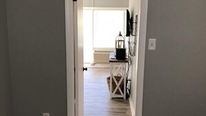 A hallway with a wooden floor leading to a room with a bed and a small table with a lamp. - Capital City Condo #1 close to Interstate, Water Park, Restaurants and Shopping (Frankfort)
