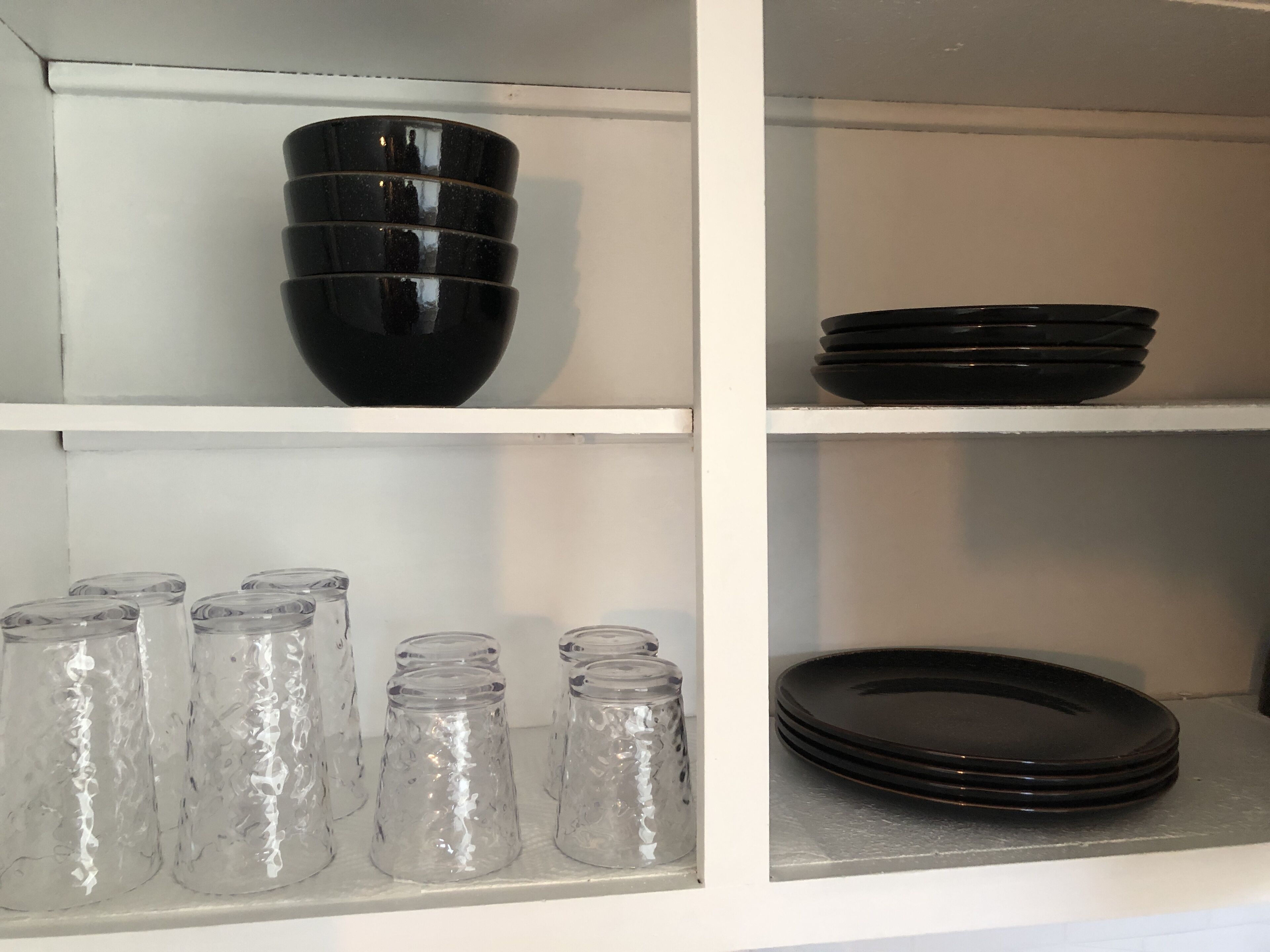 A kitchen cabinet with black bowls, plates, and clear glass jars.
