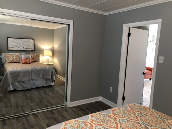 Un dormitorio con cama, mesita de noche, espejo y puerta que da a otra habitación.