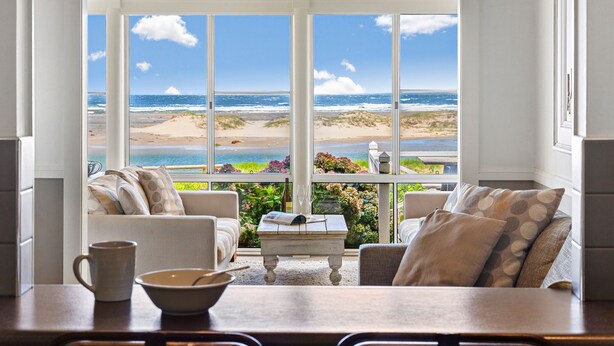 A cozy seating area with a view of the beach and ocean through large windows. - The Beach House, Gerroa, South Coast (Gerroa)