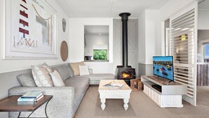 A living room with a fireplace, sofa, coffee table, and a TV. - The Beach House, Gerroa, South Coast (Gerroa)