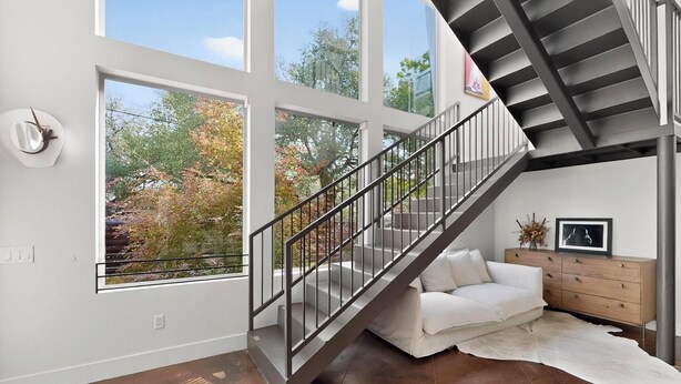 A modern interior with a staircase, large windows, a white sofa, and a wooden cabinet.