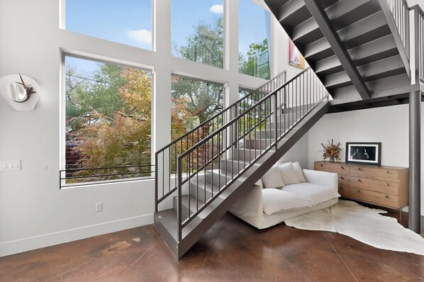 A modern interior with a staircase, large windows, a white sofa, and a wooden cabinet.