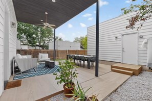 A covered patio with a ceiling fan, a dining table with chairs, a seating area with a couch, and a potted plant.