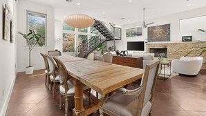 A modern interior with a dining area, staircase, living room, fireplace, and artwork.
