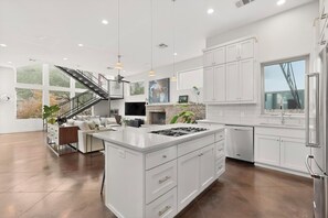 A modern kitchen with white cabinetry, a central island, and a staircase leading to a balcony.
