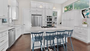 A modern kitchen with white cabinetry, stainless steel appliances, and blue bar stools.