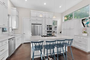 A modern kitchen with white cabinetry, stainless steel appliances, and blue bar stools.