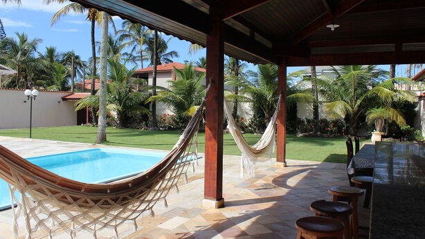 Un espacio al aire libre techado con piscina, hamacas y un bar.