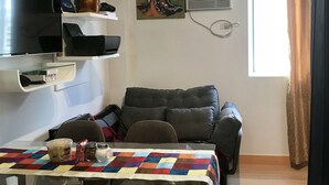 A compact living space with a dining table, chairs, a sofa, a TV, and artwork on the wall. - Happy Place at Trees Residences Fairview (Quezon City)
