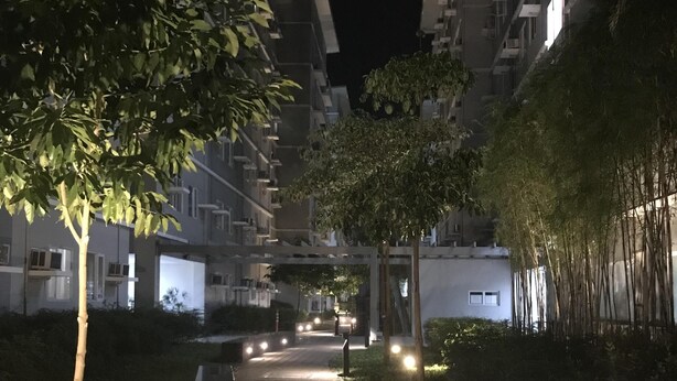 A nighttime view of a residential building with a paved pathway, trees, and illuminated windows. - Happy Place at Trees Residences Fairview (Quezon City)