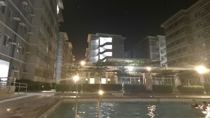 A nighttime view of a residential building complex with multiple balconies and a swimming pool area. - Happy Place at Trees Residences Fairview (Quezon City)