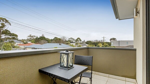 A balcony with a table and chairs, a lantern, and a view of neighboring houses and trees.