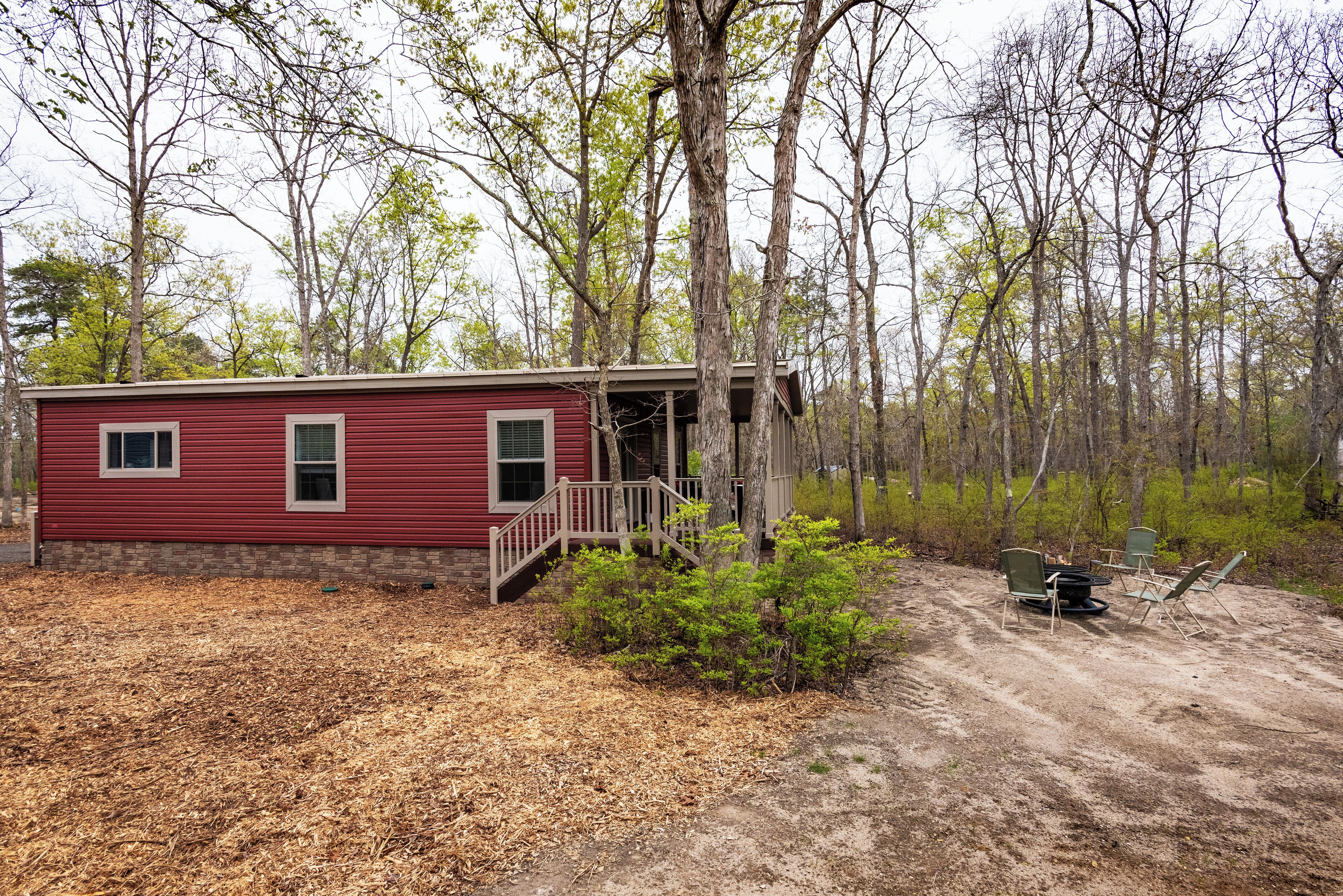A red cabin with a wooden deck and a dirt path leading to it, surrounded by trees and shrubs.