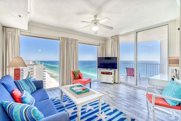 A spacious living room with a large sofa, a coffee table, and a TV. It features a balcony with a view of the ocean. - *Wonderful Views!* Gulf Front! Aug 15 - 19th open! (Panama City Beach)