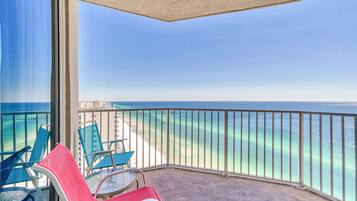 A balcony with a view of the ocean and a pier. There are chairs and a table on the balcony.