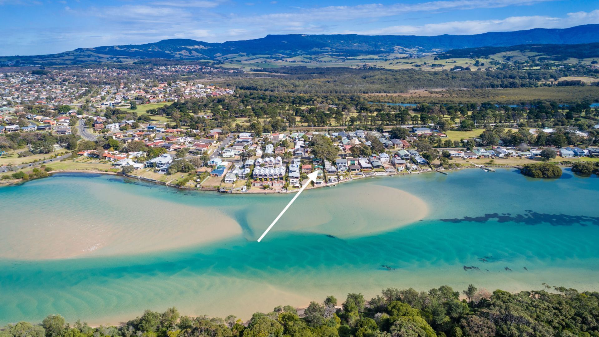 An aerial view of a coastal town with a marina, clear waters, and surrounding hills.