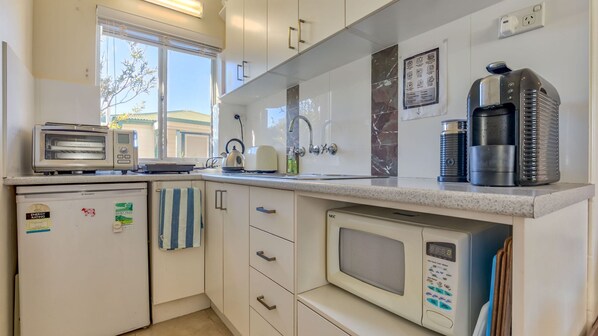 A compact kitchen with a toaster, kettle, coffee maker, and a microwave.