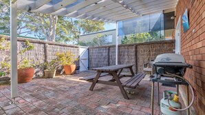 A covered patio with a grill, seating, and potted plants. - Riverside Studio, Minnamurra, South Coast (Minnamurra)