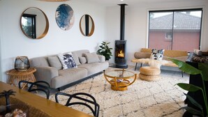 A cozy living room with a sofa, a glass coffee table, a fireplace, and a large window. - The Werri Shack, Gerringong (Gerringong)