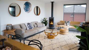 A cozy living room with a sofa, a glass coffee table, a fireplace, and a large window.