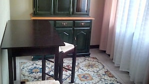 A room with a dark wooden table and a matching chair, a green cabinet with multiple drawers, and a patterned rug on the floor.
