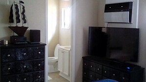 A bedroom with a bed, a dresser, a television, and a bathroom visible through an open door.